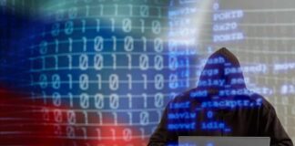 A hooded figure working on a laptop with binary code in the background
