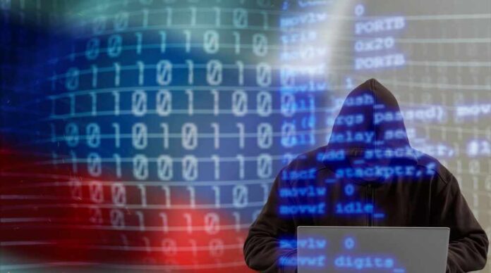 shutterstock_2203813797.jpg A hooded figure working on a laptop with binary code in the background