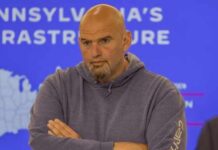 Man in a hoodie with arms crossed, looking serious in front of a presentation background