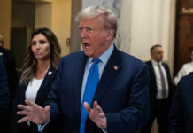 A man in a suit passionately speaking in a government building with a woman beside him