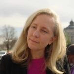 A woman with blonde hair speaking outdoors with a city building in the background