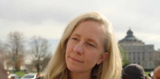 A woman with blonde hair speaking outdoors with a city building in the background