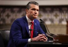 Man in a blue suit sitting at a table during a government hearing