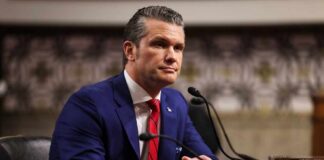 Man in a blue suit sitting at a table during a government hearing