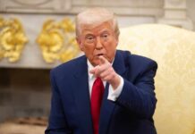 A man in a blue suit and red tie pointing while seated