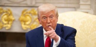 A man in a blue suit and red tie pointing while seated