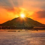 An ancient pyramid at sunset with people sitting nearby