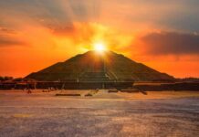 An ancient pyramid at sunset with people sitting nearby