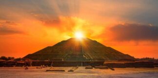An ancient pyramid at sunset with people sitting nearby