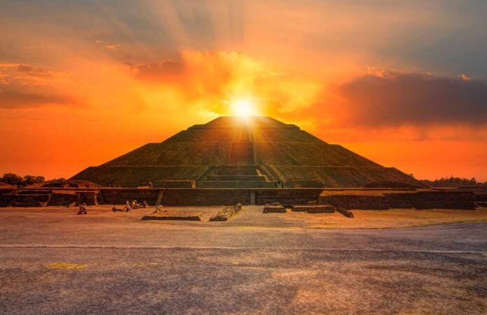An ancient pyramid at sunset with people sitting nearby