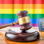 A wooden gavel on a table with a rainbow flag in the background