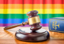 A wooden gavel on a table with a rainbow flag in the background