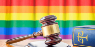 A wooden gavel on a table with a rainbow flag in the background