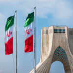 Three Iranian flags in front of the Azadi Tower against a blue sky