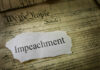 A torn piece of paper with the word 'Impeachment' on an old document background