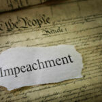A torn piece of paper with the word 'Impeachment' on an old document background
