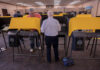 Individuals casting votes at a polling station with electronic voting machines