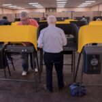 Individuals casting votes at a polling station with electronic voting machines
