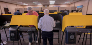 Individuals casting votes at a polling station with electronic voting machines