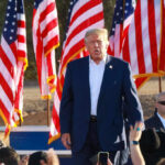 A speaker at a political rally surrounded by American flags and an engaged crowd