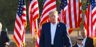 A speaker at a political rally surrounded by American flags and an engaged crowd
