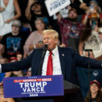 A speaker at a political rally addressing a large crowd with enthusiasm