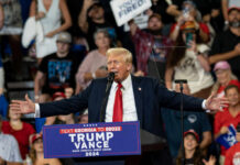 A speaker at a political rally addressing a large crowd with enthusiasm