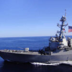 A naval destroyer sailing in the ocean with an American flag