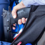 A hand holding a handgun partially visible in a backpack