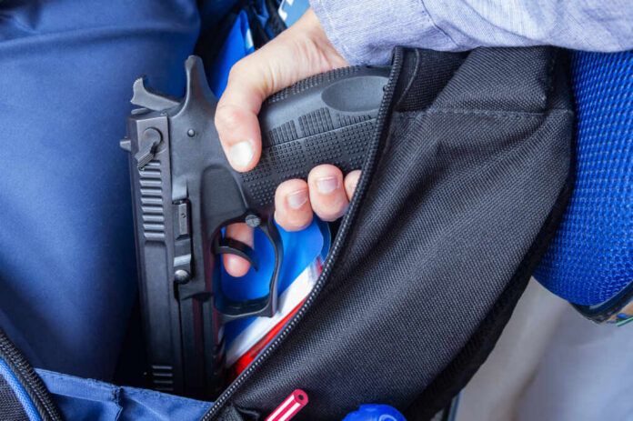 School,Shootings,,Gun,Control,,Bullying,And,Gun,Violence.,Social,Issues A hand holding a handgun partially visible in a backpack