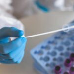 Healthcare professional holding a swab next to a tray of sample vials