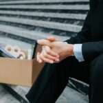 A person in business attire sitting on steps with a cardboard box of belongings