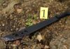 A machete with blood on it lying on the ground next to an evidence marker