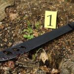 A machete with blood on it lying on the ground next to an evidence marker