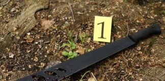 A machete with blood on it lying on the ground next to an evidence marker