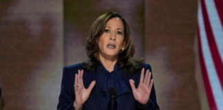 A woman in formal attire delivering a speech at a podium with an American flag in the background