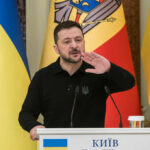 Ukrainian leader speaking at a podium with national flags in the background