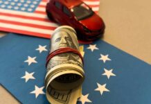 A rolled bundle of cash on a blue background with stars, next to a small red toy car and an American flag.
