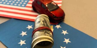 A rolled bundle of cash on a blue background with stars, next to a small red toy car and an American flag.