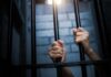 Hands gripping prison bars in a dimly lit environment