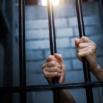 Hands gripping prison bars in a dimly lit environment