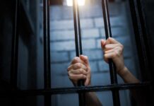 Hands gripping prison bars in a dimly lit environment