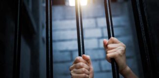Hands gripping prison bars in a dimly lit environment