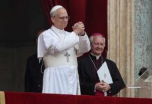 A religious leader in white robes gestures during a public address