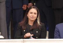 Spy Chief RESIGNS Amid Political Turmoil! A woman in a black blazer sitting outdoors, holding a water bottle