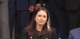 A woman in a black blazer sitting outdoors, holding a water bottle