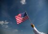 A hand holding an American flag against a clear blue sky