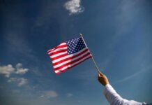 A hand holding an American flag against a clear blue sky