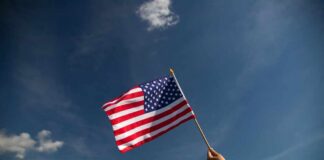 A hand holding an American flag against a clear blue sky