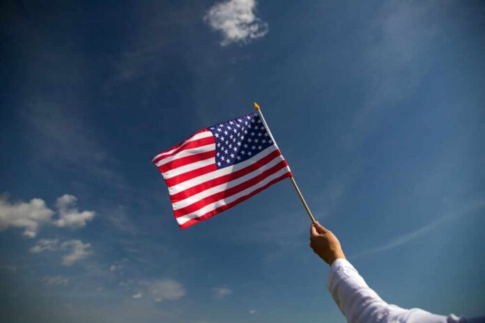 shutterstock_2640047429.jpg A hand holding an American flag against a clear blue sky